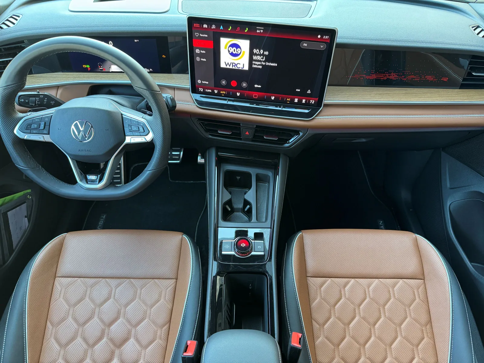 Une vue aérienne de l'habitacle orienté vers le conducteur du VW Tiguan SEL R-Line. Des pédales recouvertes d'acier inoxydable, un volant inspiré de la course et une disposition semblable à celle d'un cockpit qui embrasse le conducteur signalent l'intention de conception de l'habitacle. Le cuir brun ambré qui éclabousse de couleur depuis les sièges jusqu'aux portes et au tableau de bord apporte une touche finale.