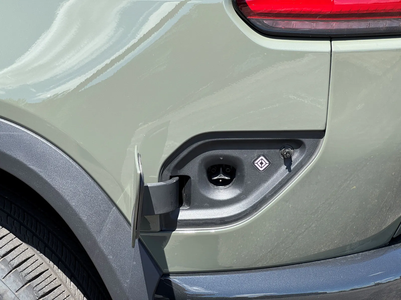 Un port de recharge ouvert pour véhicule électrique est illustré. À droite du port de chargement se trouve le logo en forme de losange de Rivian.